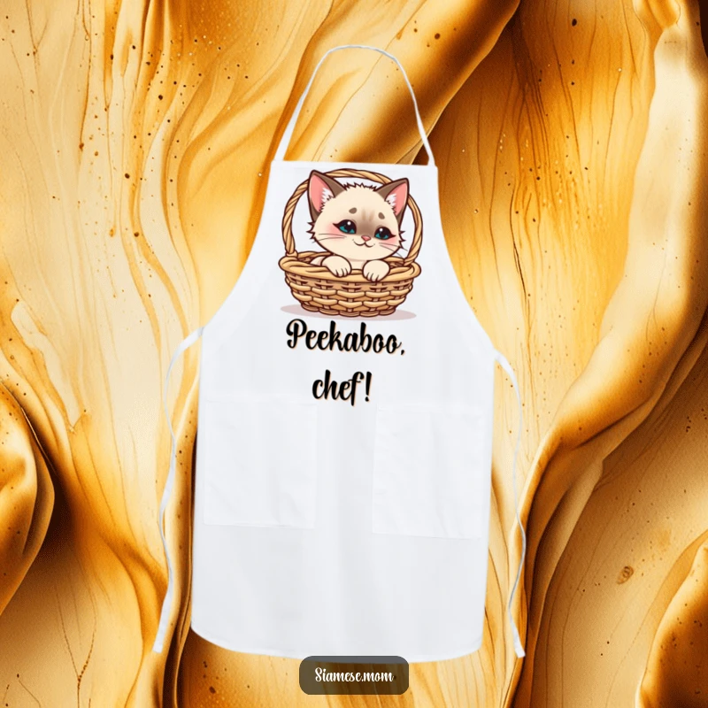 Funny Siamese Cat Apron, kawaii cat peeking from a basket with a smirk, ideal accessory for funny kitchen gifts.