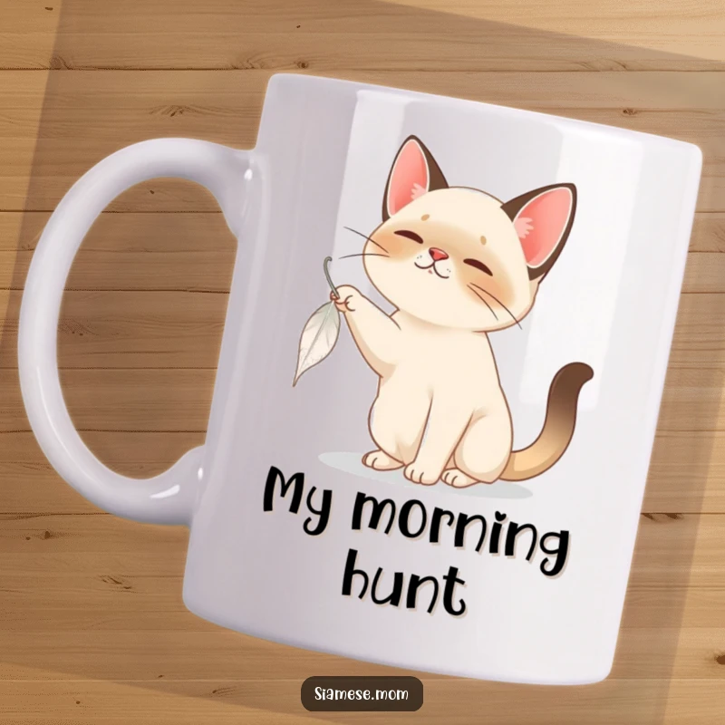 Funny Siamese Cat Mug: A curious Siamese cat playfully bats at a slowly falling feather, showcasing feline focus and fun.