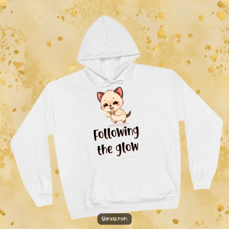 Funny Siamese cub giggling while chasing a shimmering light beam, a cozy and humorous hoodie for playful cat lovers.