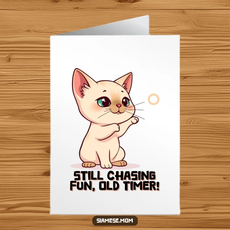 Funny Free Printable Birthday Card: Siamese cat character intensely batting at a projected red laser dot, full of playful energy.