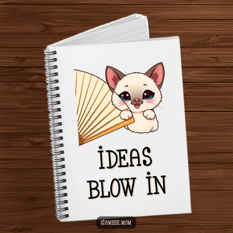 Funny happy Siamese cat peeking from behind a large, cheerful fan, on the cover of a notebook.