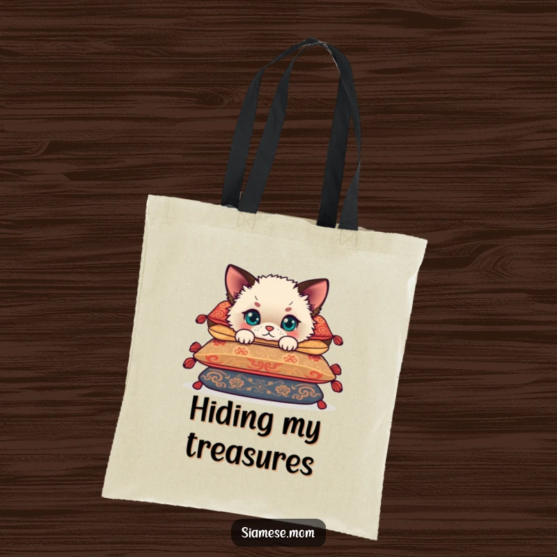 Funny Siamese cub peeking humorously from behind cushions, a cute kitten on a durable tote bag for stylish, funny shopping.